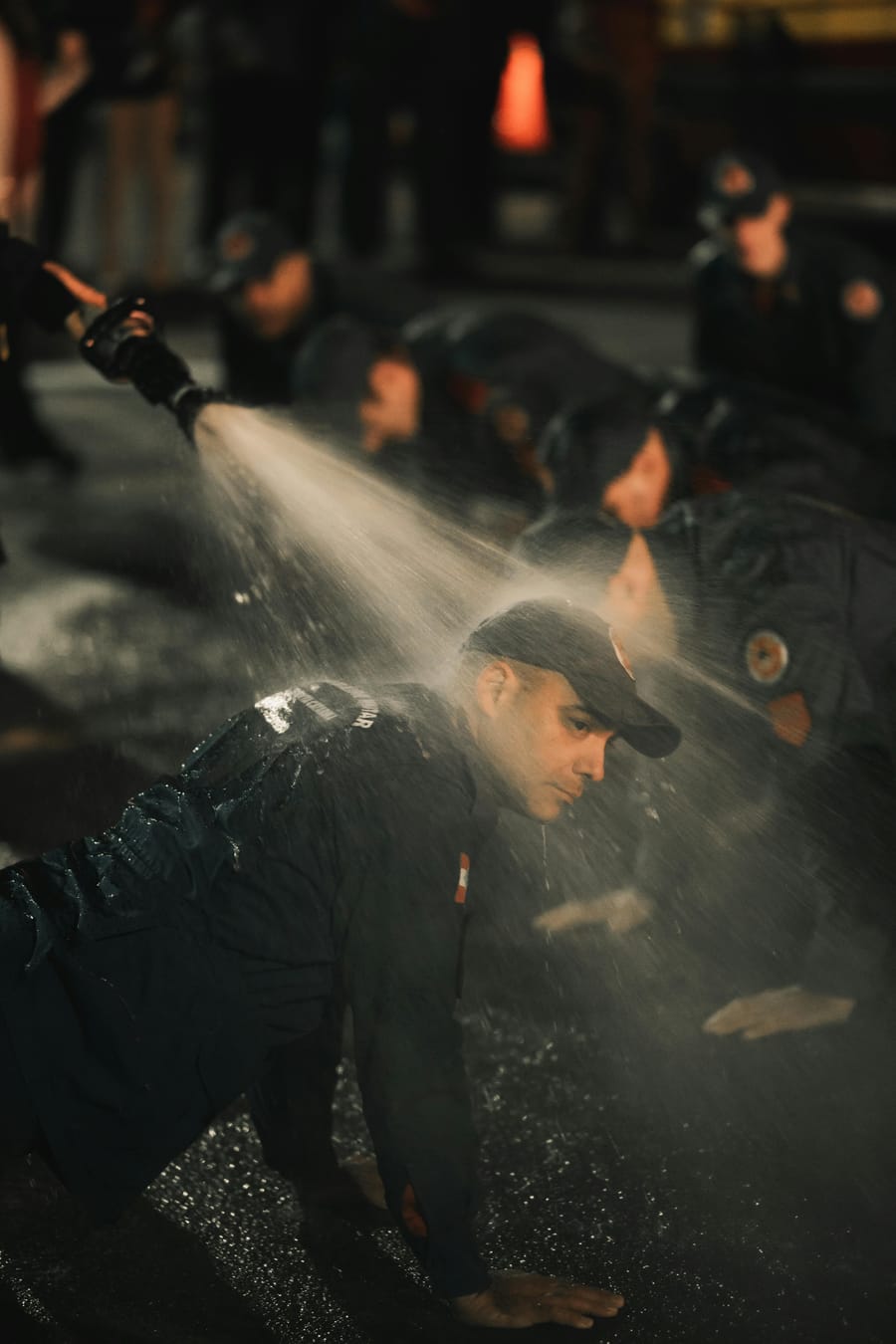 Crew in firefighting gear running a night-time water hose drill.