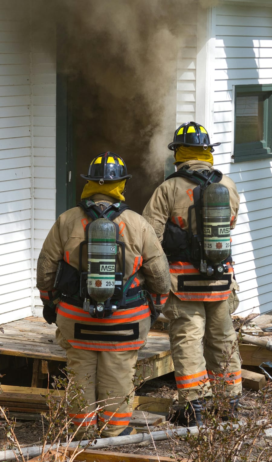 Two students in full safety kit entering a smoke-filled training building.